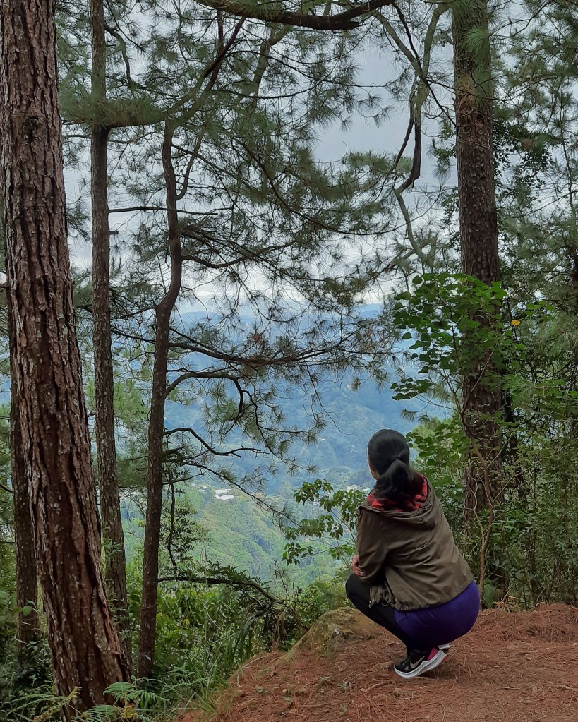 Person sitting along a hiking path overlooking a mountain view