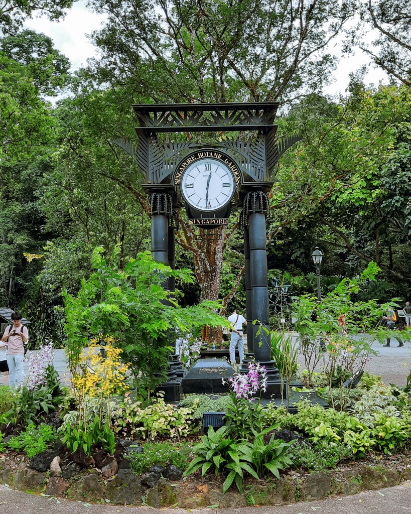 A decorative clock tower at Singapore Botanic Gardens, surrounded by vibrant plants and flowers.
