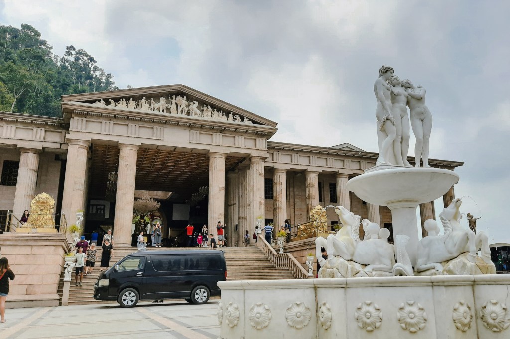The Temple of Leah, a grand neoclassical structure, featuring impressive columns and a staircase leading to its entrance, surrounded by visitors and a black van parked in front.