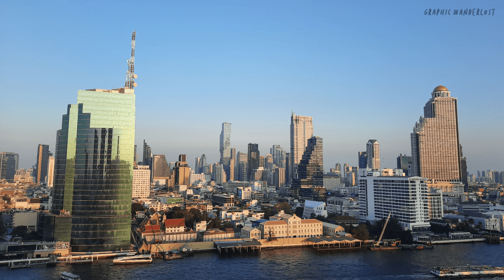 A panoramic view of Bangkok skyline showcasing various modern skyscrapers and buildings along the Chao Phraya River under a clear blue sky.