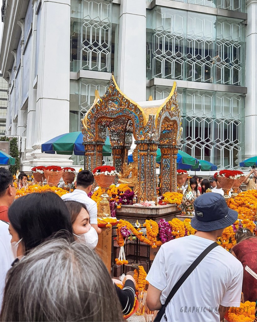 Crowd gathered at a colorful shrine adorned with flowers in Bangkok, showcasing a vibrant atmosphere of worship.