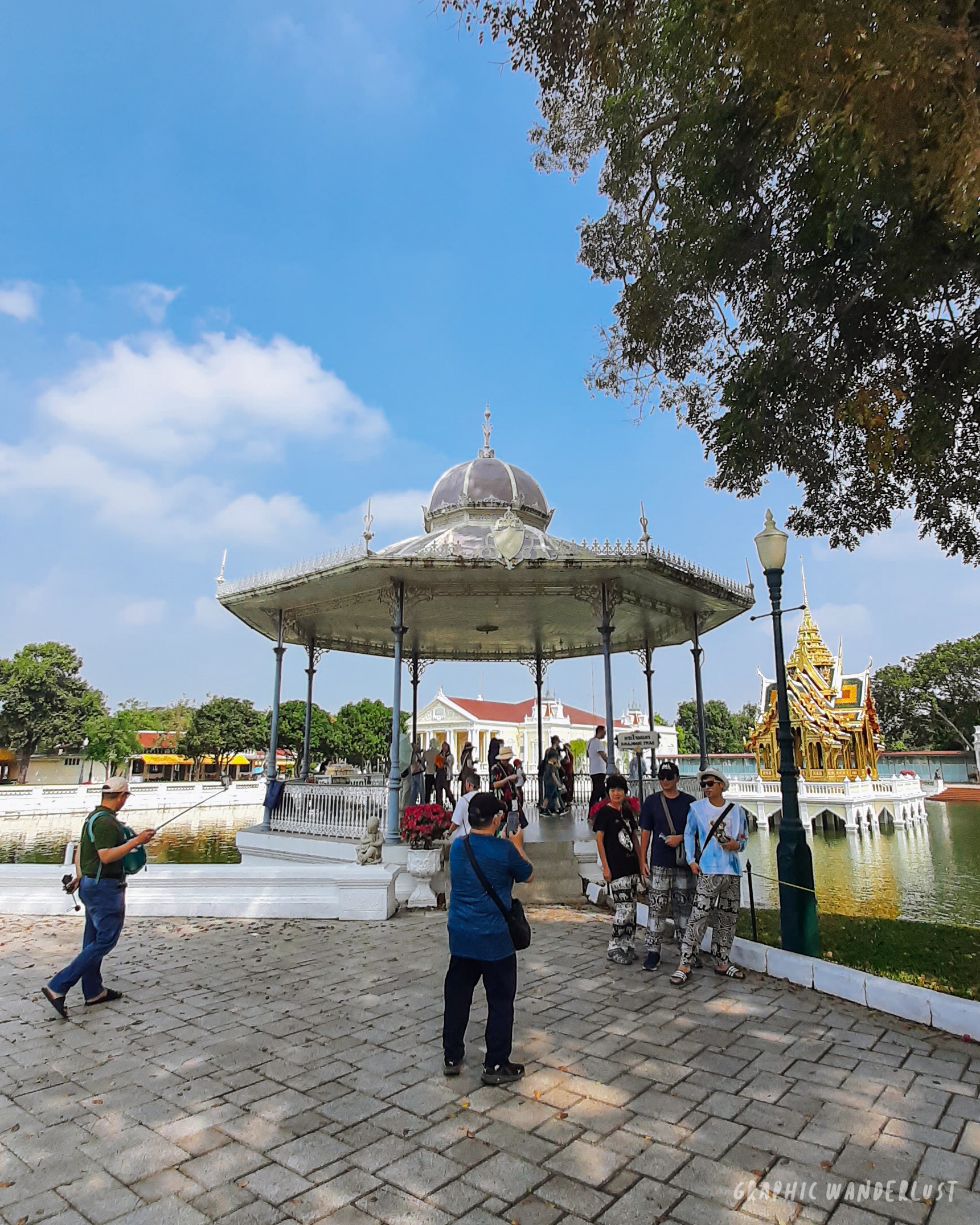 People gathering inside and around a pavilion beside a man-made lake in Bang Pa-in Palace