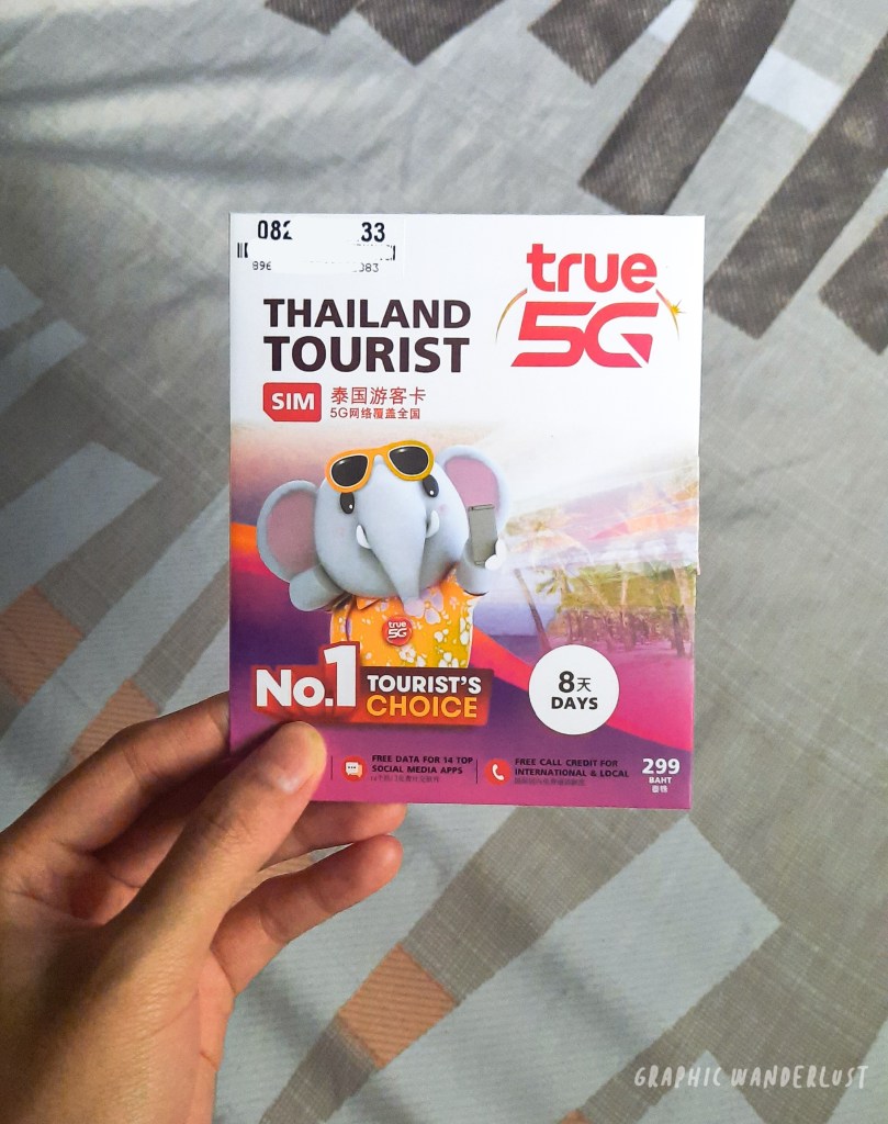 A hand holding a SIM card package for tourists in Thailand, featuring an elephant character, with colorful design and details about data and call options.