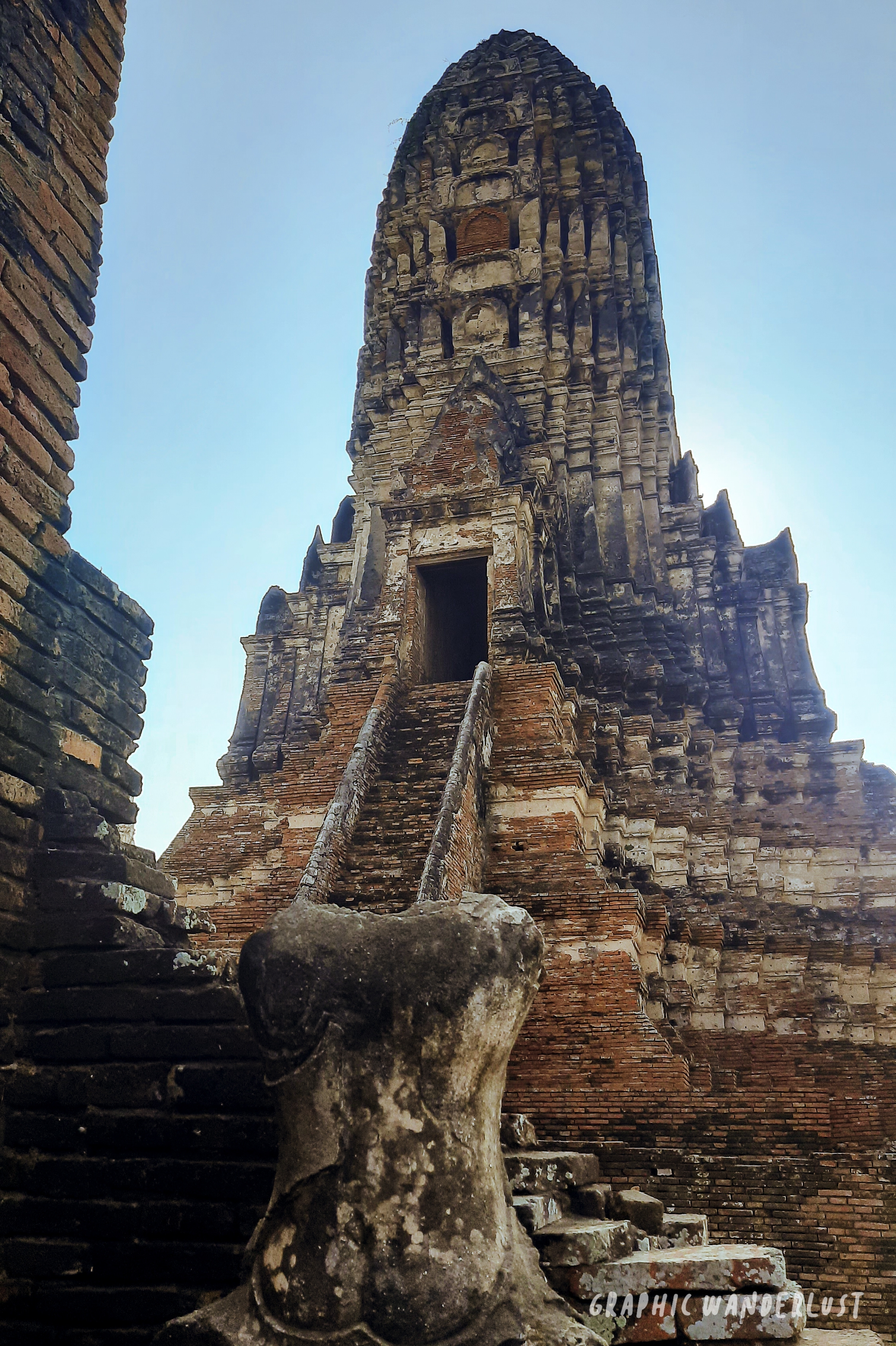 Main prang of Wat Chaiwatthanaram in the background and a headless Buddha image in the forefront