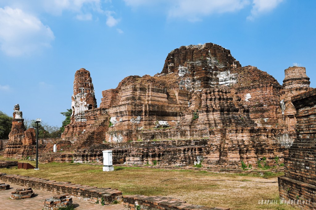 Ruins of an ancient temple structure in Ayutthaya, Thailand, featuring weathered brick walls and spires under a blue sky.