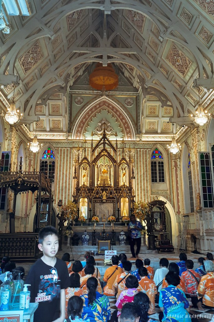 Interior of Wat Niwet Thammaprawat featuring a Neo-Gothic design, with a group of visitors seated on the floor and a young boy walking by.