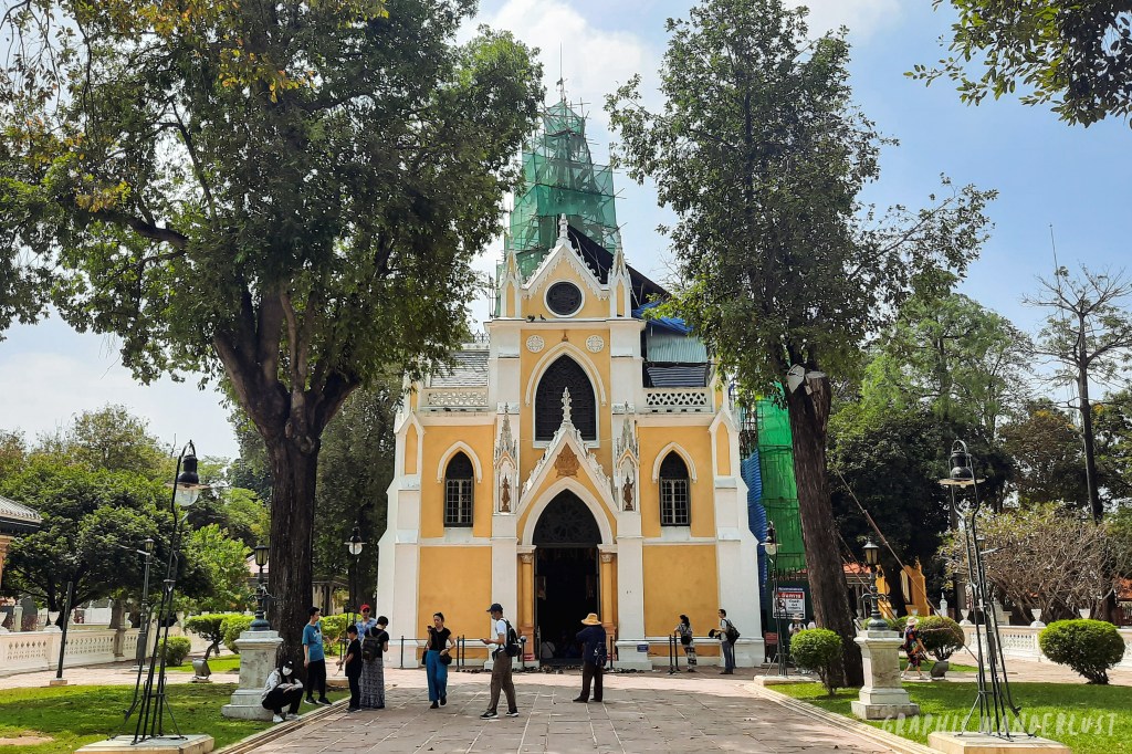 Neo-Gothic architectural style royal Buddhist temple, Wat Niwet Thammaprawat, with trees and visitors in the foreground.