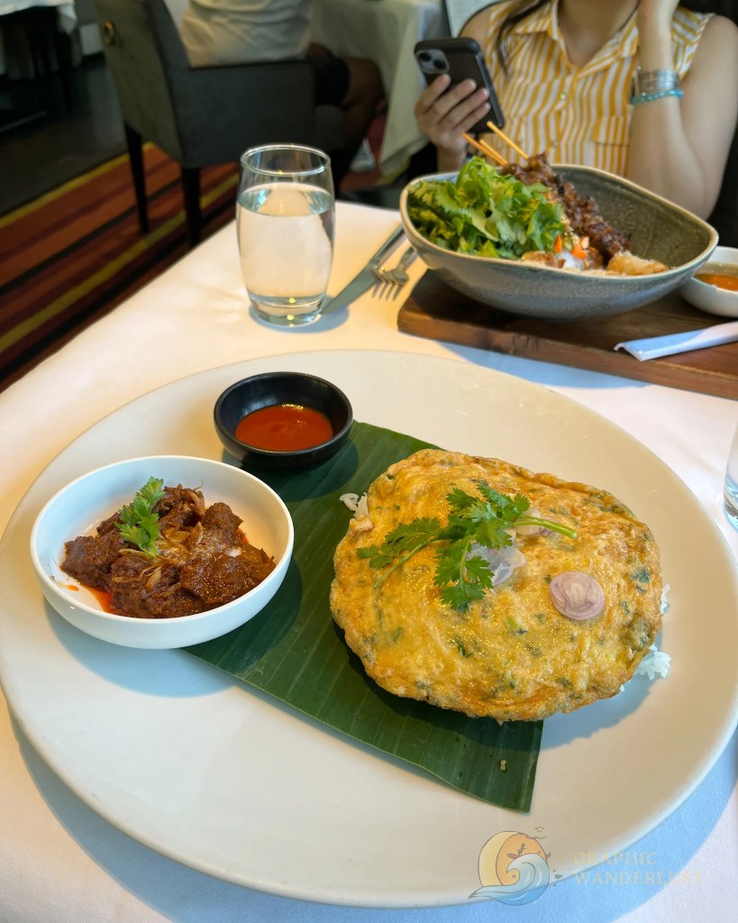 A plate of food featuring a large omelette garnished with herbs, served with a side of beef dish and dipping sauce at a dining establishment.
