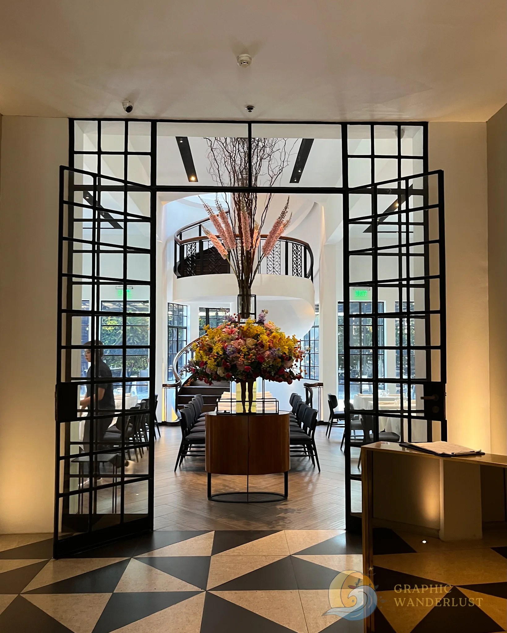 Interior of a modern dining establishment featuring a floral centerpiece, geometric patterned flooring, and stylish furnishings.