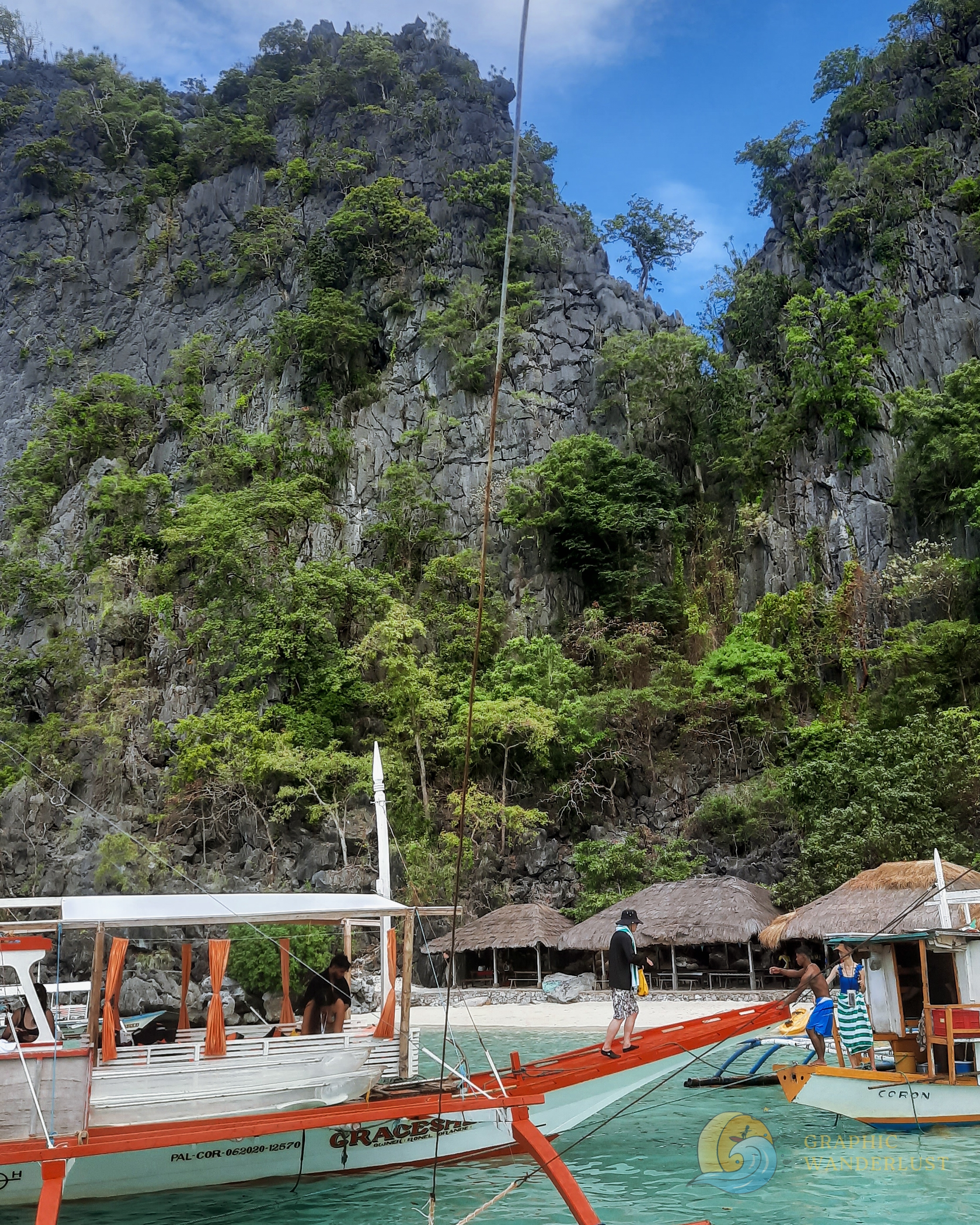 White sand beach towered over by a large karst cliff and with tourist boats docking at its shore