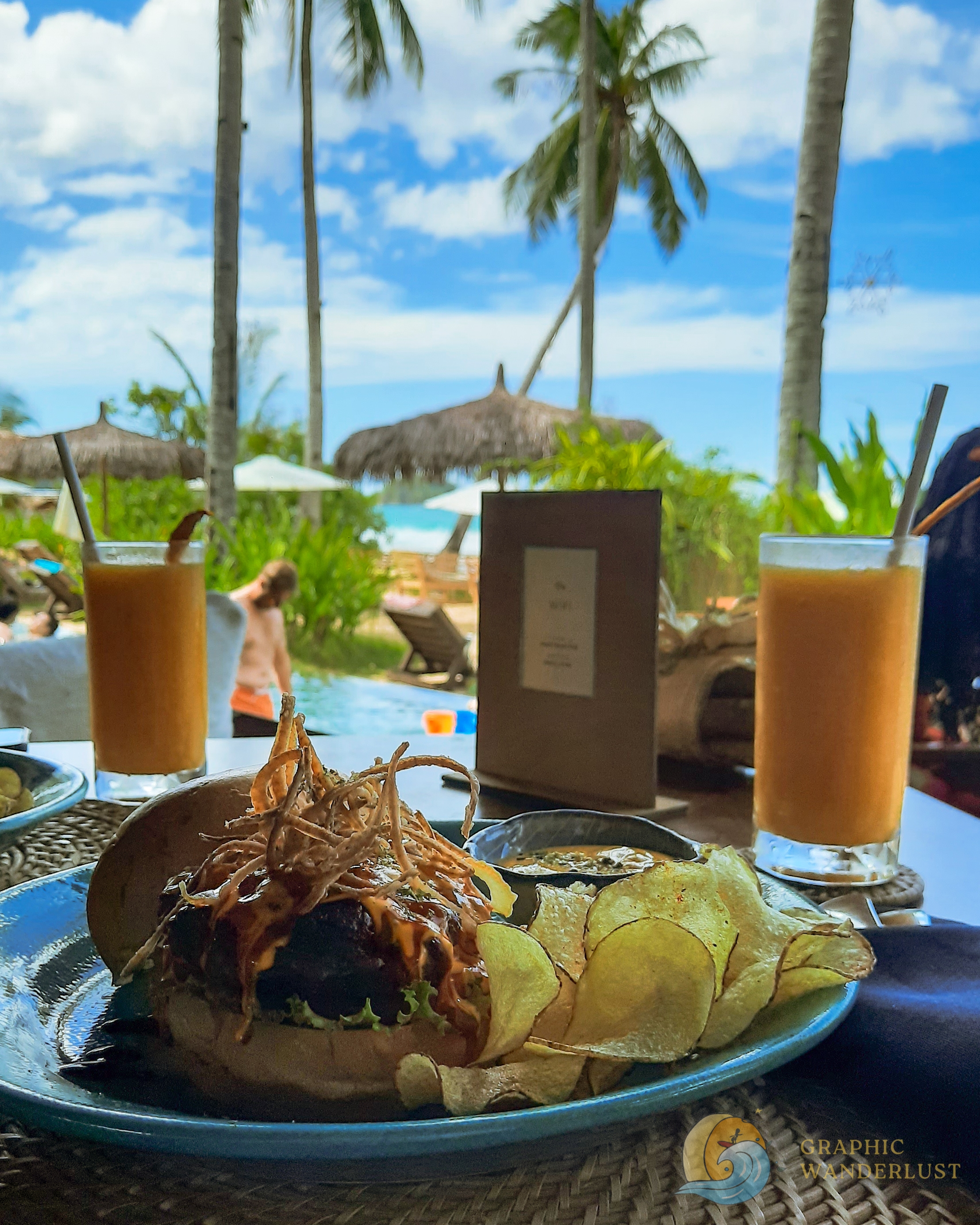 Serving of burger and fruit shake with a background of a pool and beach