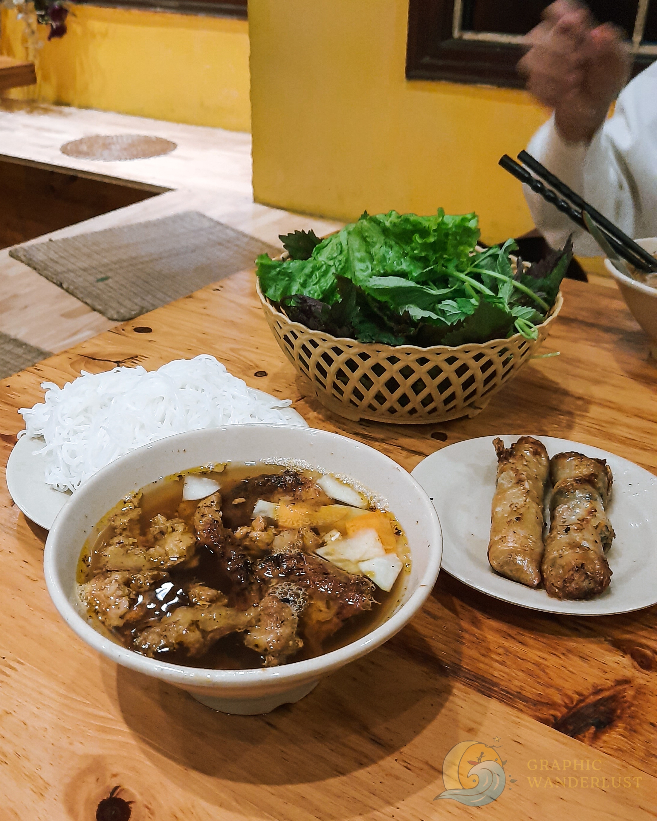 Serving of bun cha with a side dish of fresh vegetables and spring rolls in Bun Cha Ta