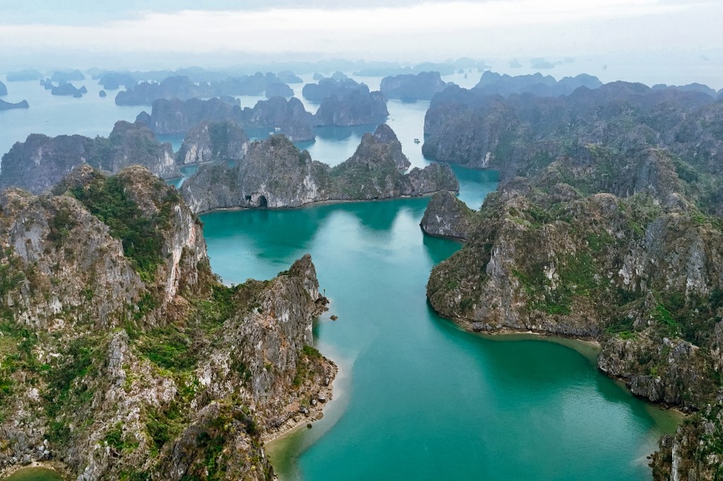 Aerial view of Ha Long Bay with limestone karsts and turquoise waters under a cloudy sky.