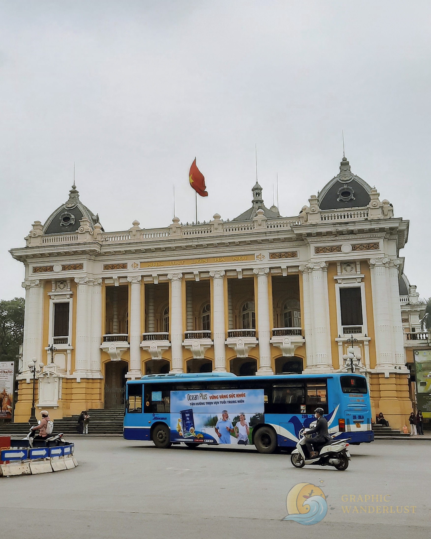 French colonial building with the Vietnamese flag on top of it and a bus in front of it