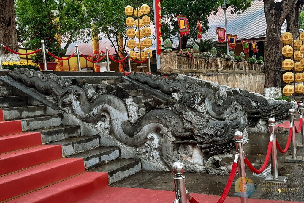 A close-up of an intricately carved stone dragon sculpture along a staircase, adorned with festive decorations and red ropes.