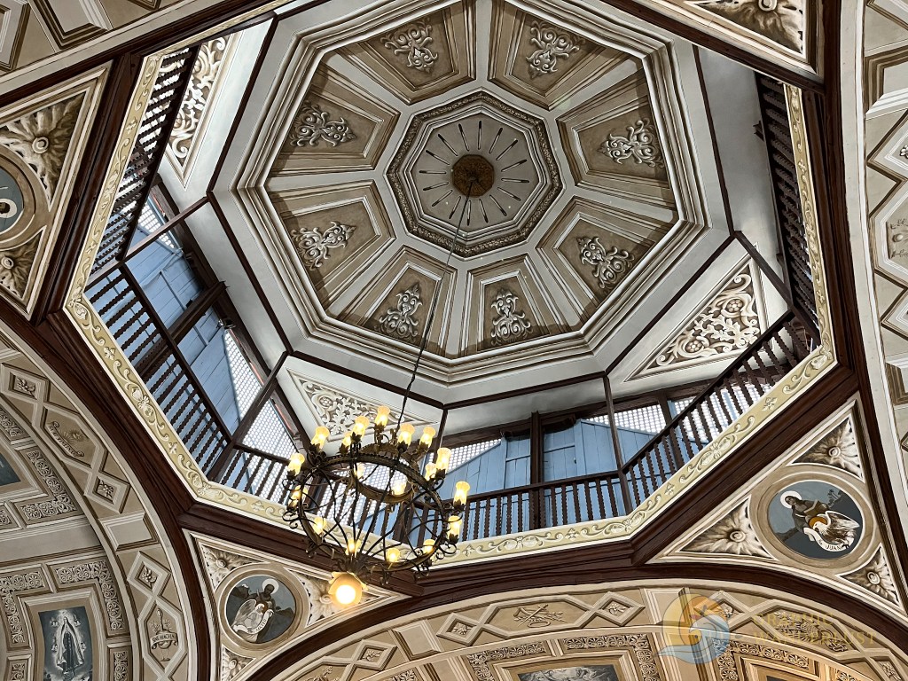 View of the intricately designed ceiling with an octagonal shape, featuring decorative details and a chandelier, inside a historic building.