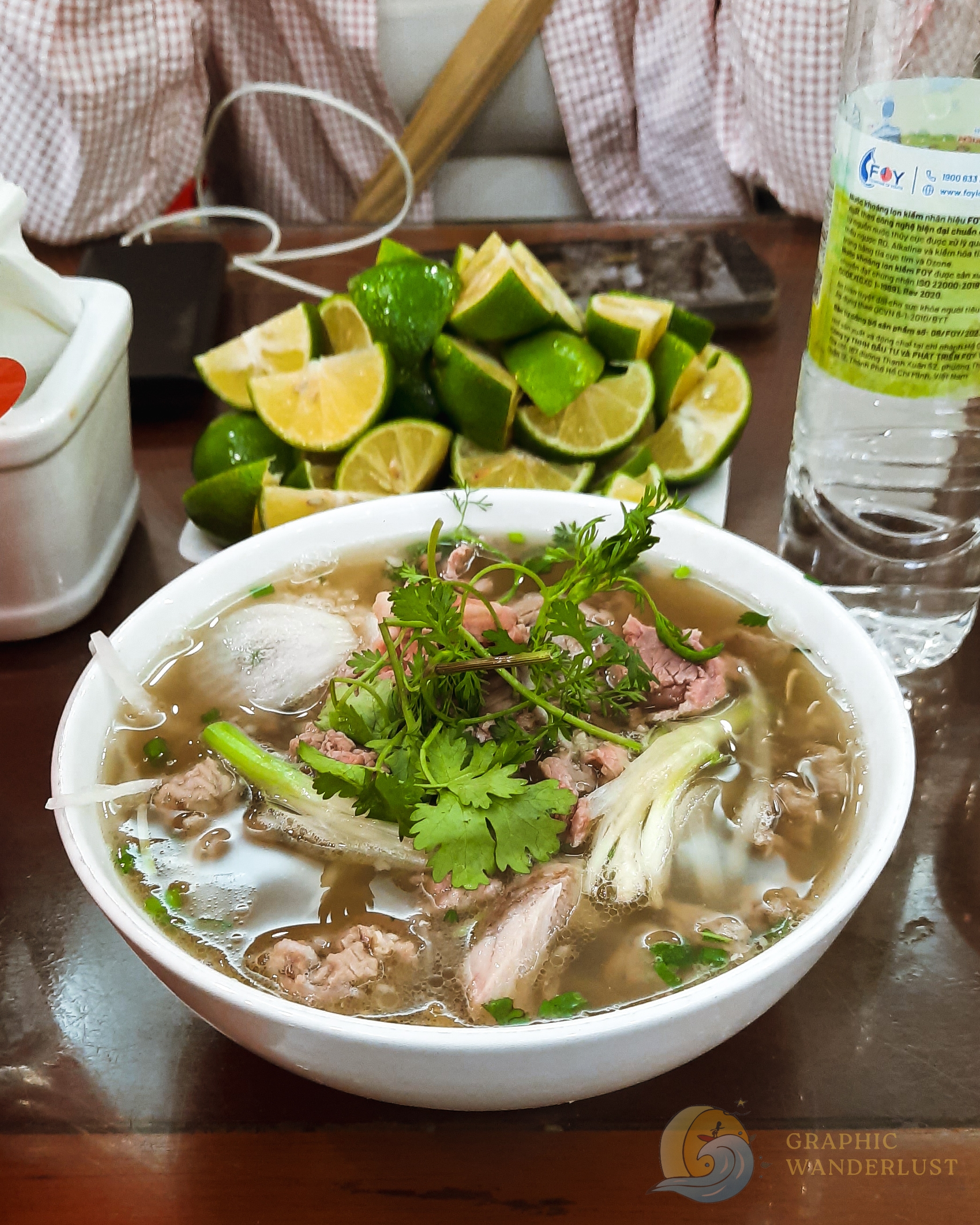 Bowl of pho with sliced limes in front of it