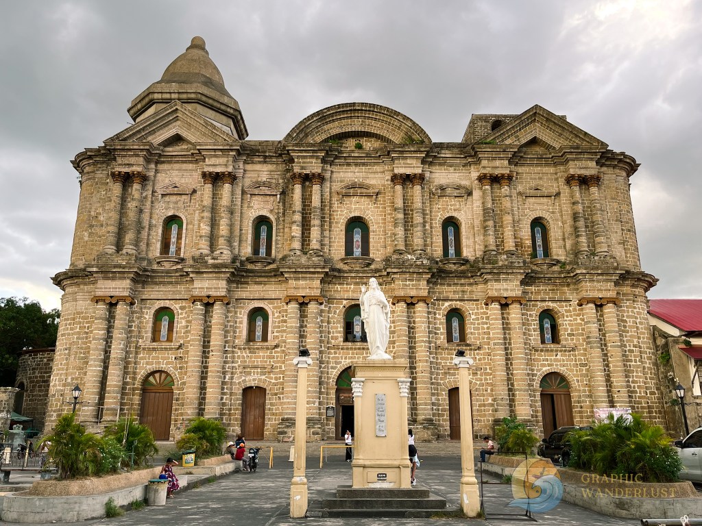 Facade of the Taal Basilica, featuring intricate architectural details and a statue of the Virgin Mary at the forefront.