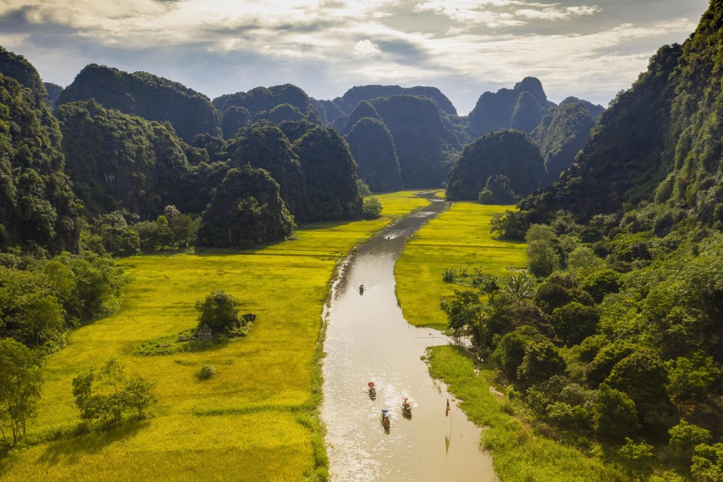 A scenic view of a river winding through lush green fields and towering limestone mountains in northern Vietnam, capturing the natural beauty of the region.