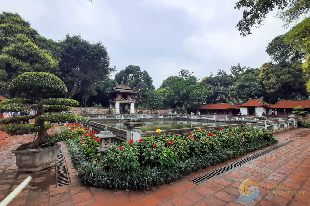 A serene view of the Temple of Literature in Hanoi, Vietnam, showcasing manicured gardens, a lotus pond, and traditional architecture under cloudy skies.