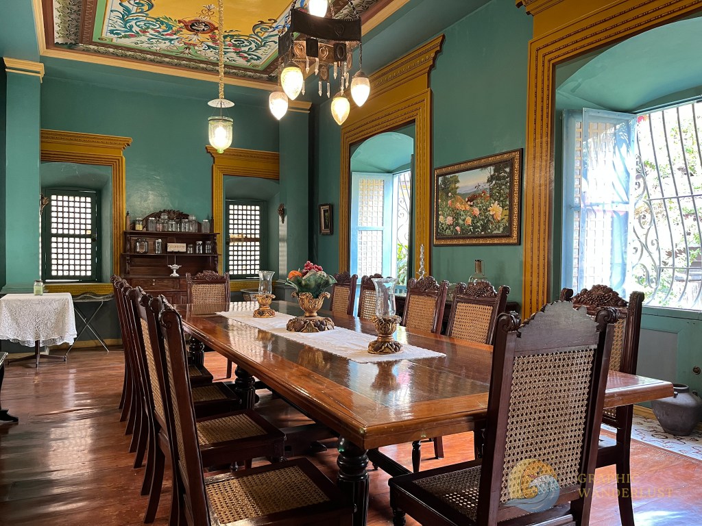 Interior of a Spanish colonial house featuring a long wooden dining table surrounded by chairs, adorned with a floral centerpiece and traditional decor.