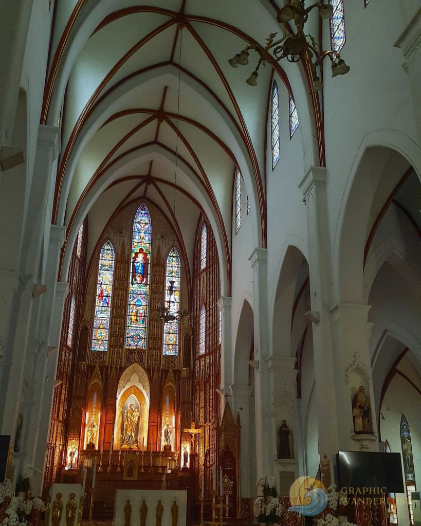 Interior view of St. Joseph Cathedral in Hanoi, featuring tall arches, stained glass windows, and an ornate altar with religious figures and decorations.