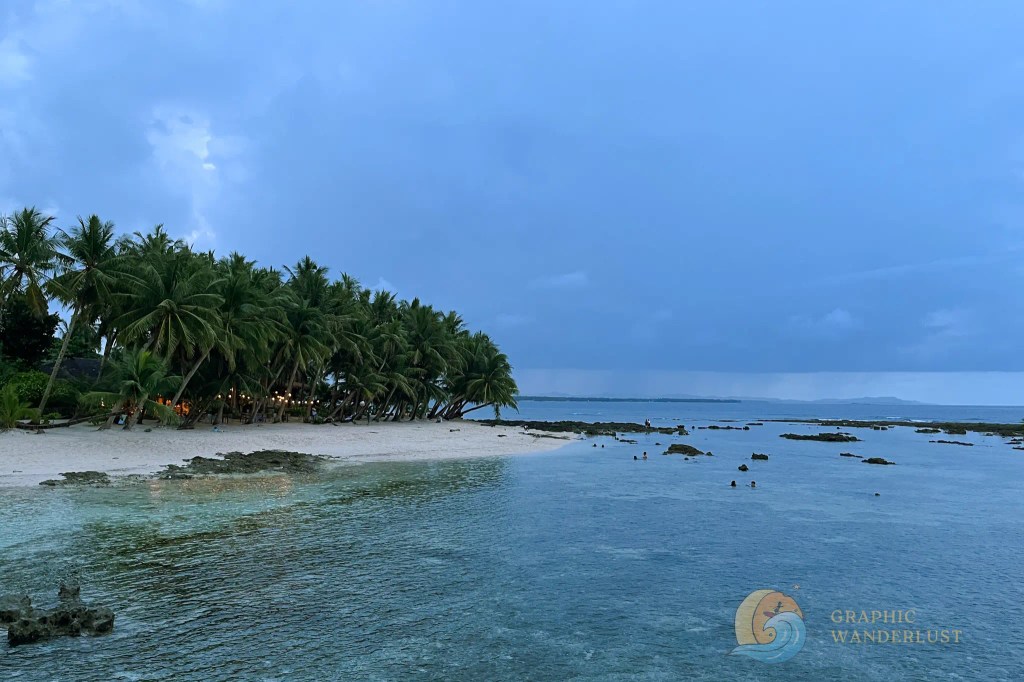 Scenic view of a tranquil beach in Siargao with palm trees, clear waters, and a cloudy sky.