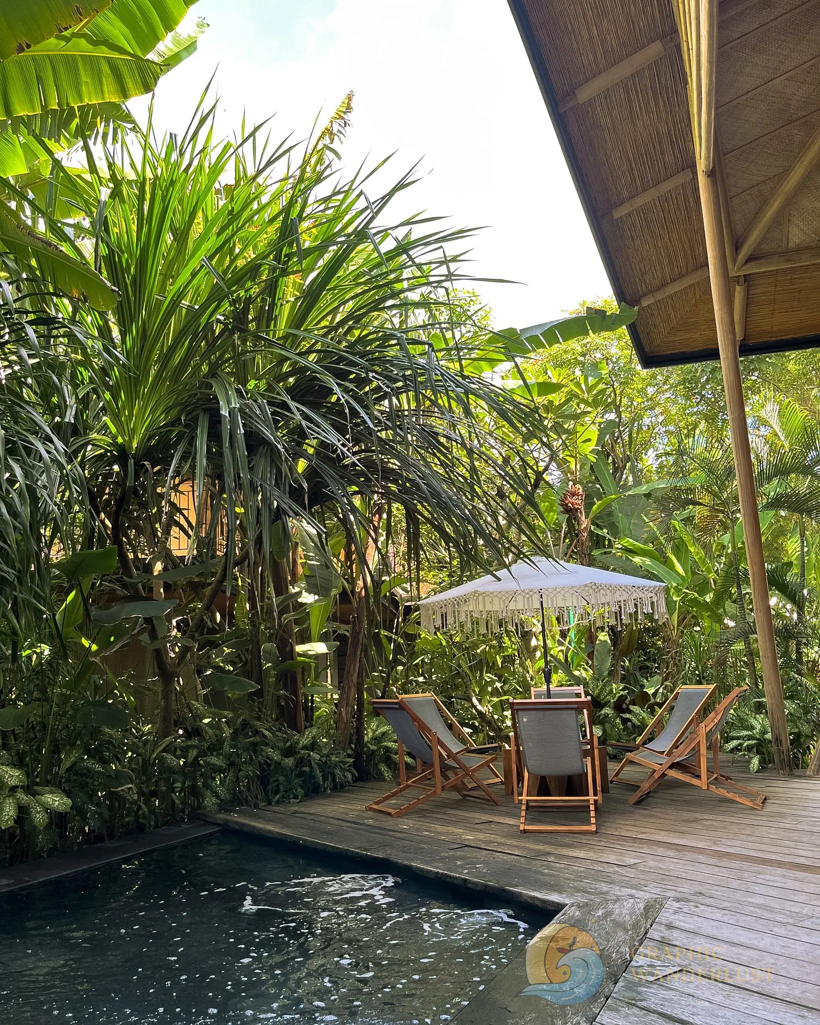 A group of beach chairs circled around an umbrella beside a pool surrounded by lush tropical plants