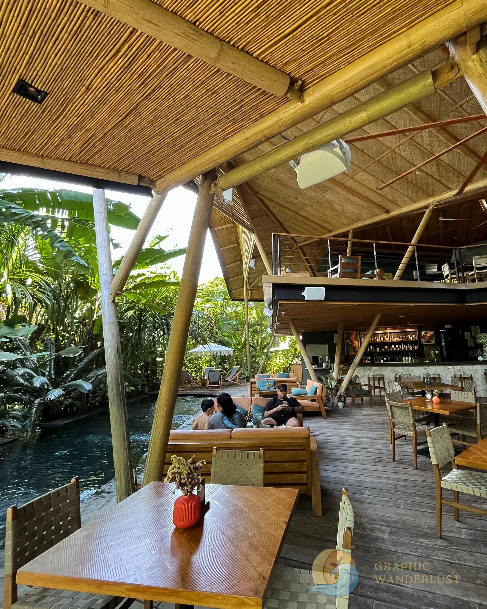 An interior view of a tropical-inspired beach resort restaurant with bamboo architecture and a pool at the side