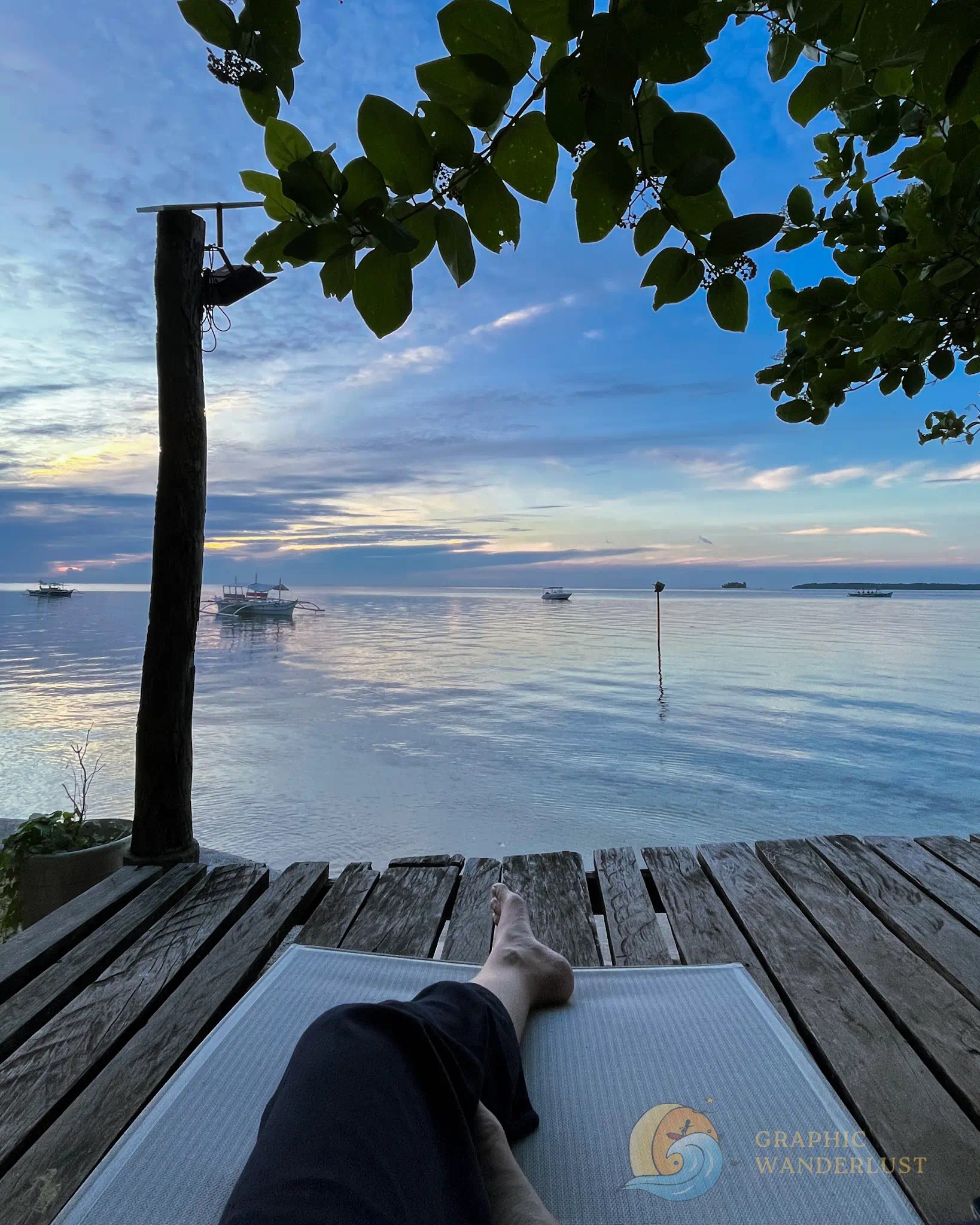 A POV of a person lounging in front of a beach with calm waters and paster-colored sky.