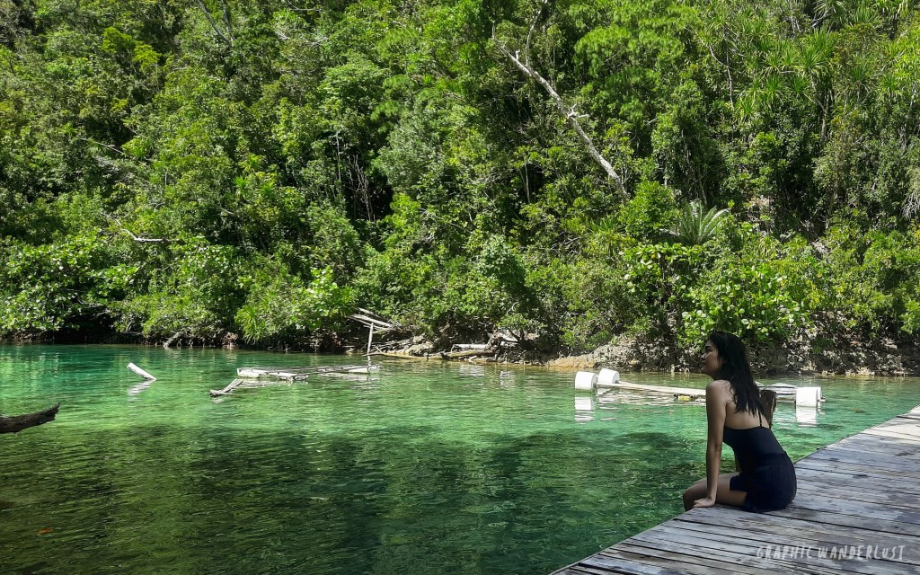 A person sitting on a wooden dock by a clear, green lagoon surrounded by lush greenery in Siargao.