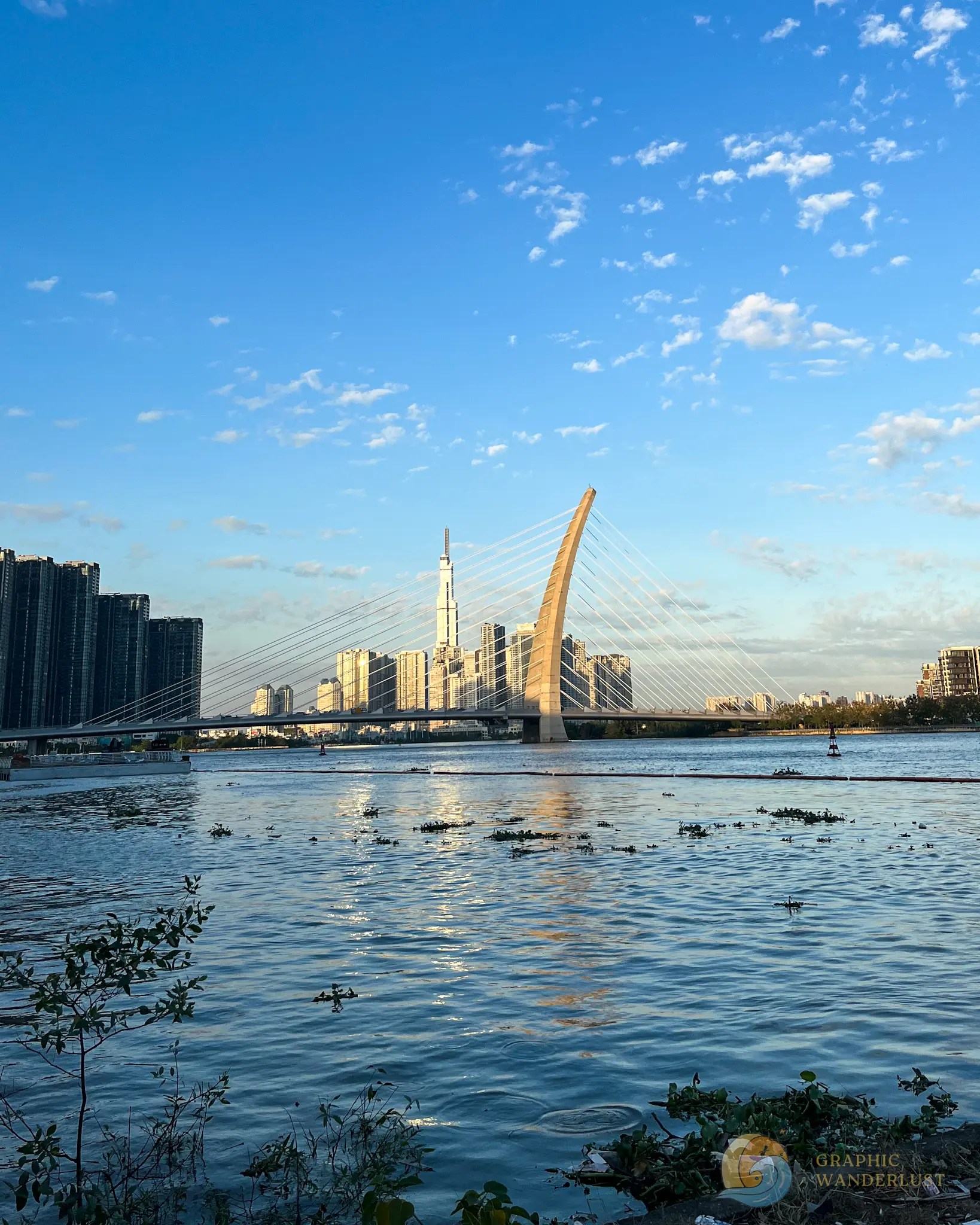 A cable-stayed bridge on top of a river with a background of a city skyline during a clear afternoon. 