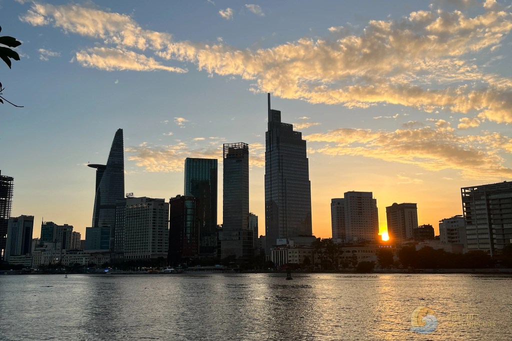 Sunset view of a skyline with various skyscrapers reflecting in the water, with clouds scattered in the sky.