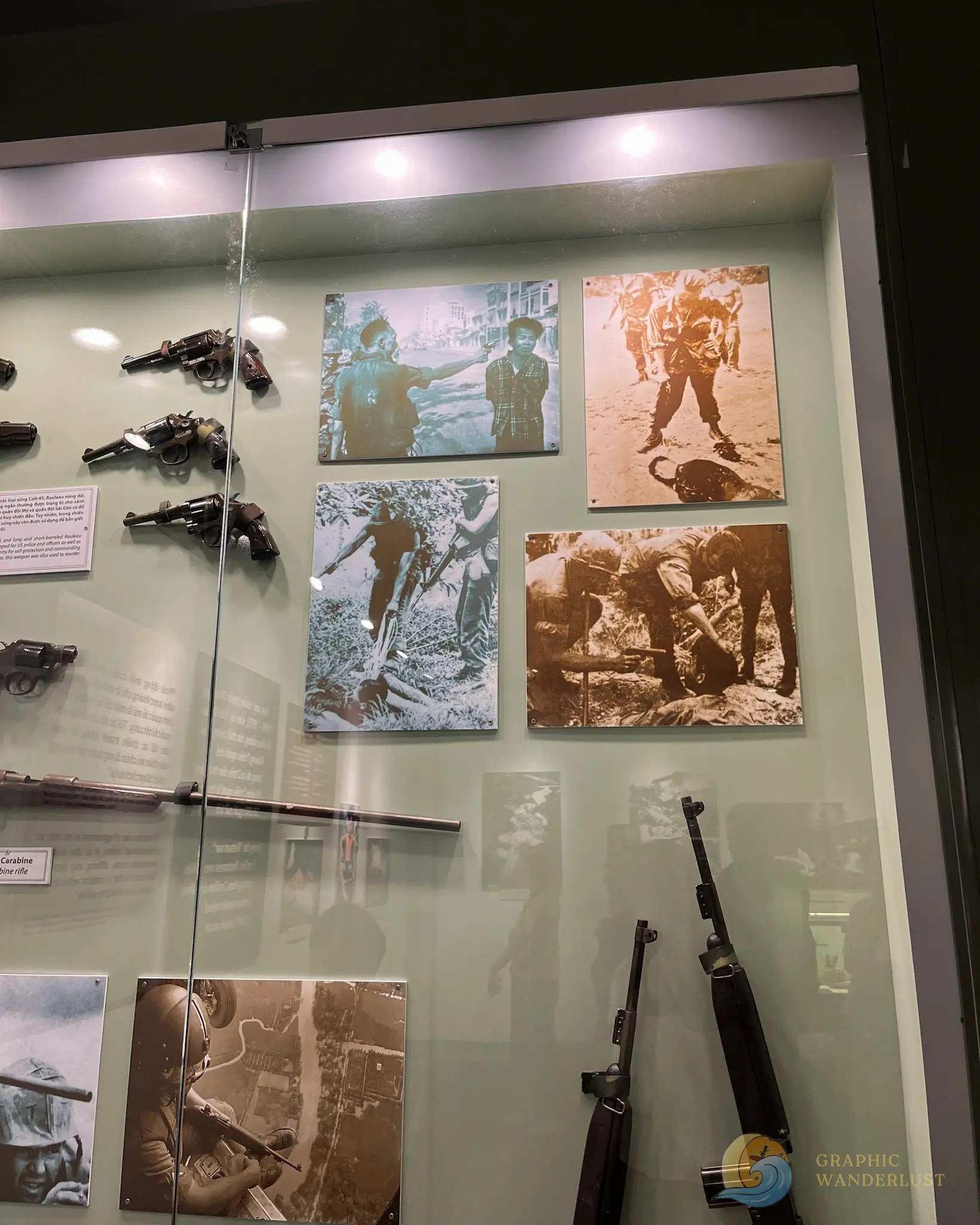 A display of graphic photographs encased in glass along with various guns.