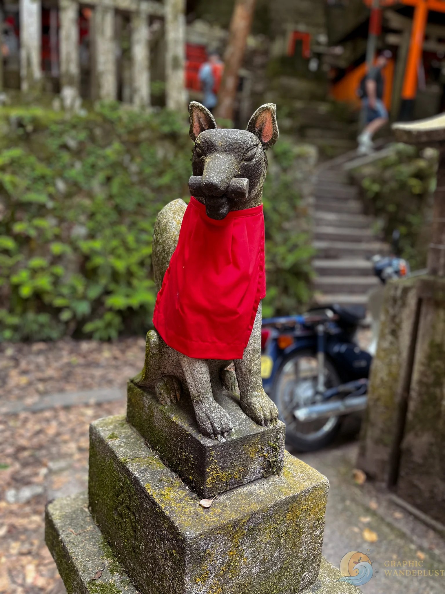 A stone fox statue, holding a scroll in its mouth and wearing a red bib around its neck.