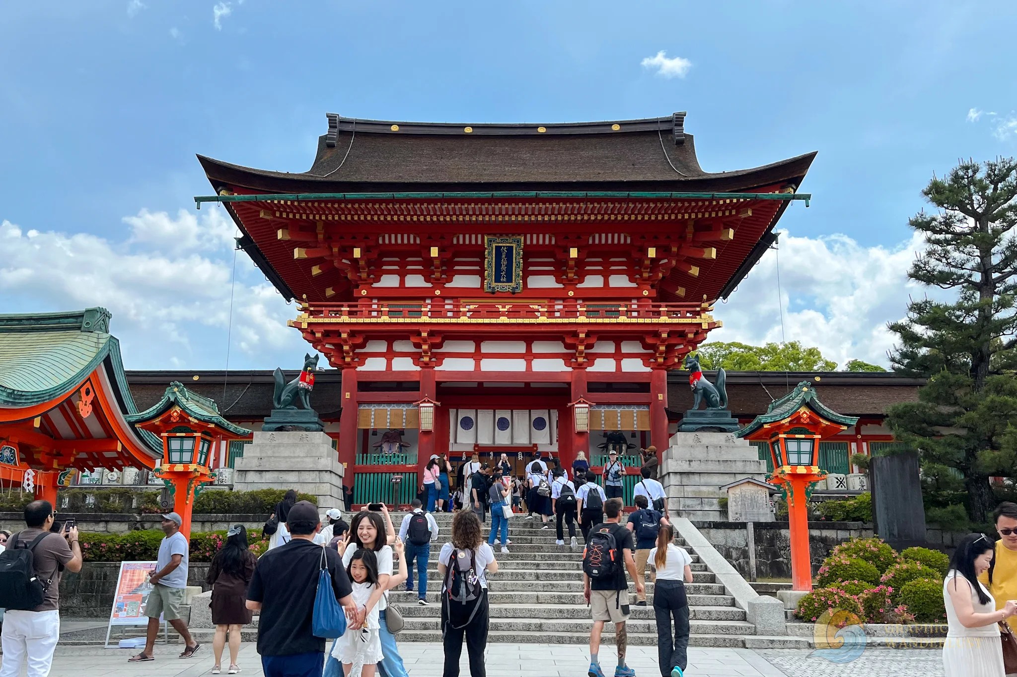 A big striking red building in traditional Japanese architecture with a flight of stairs leading to its entrance and surrounded by tourists.