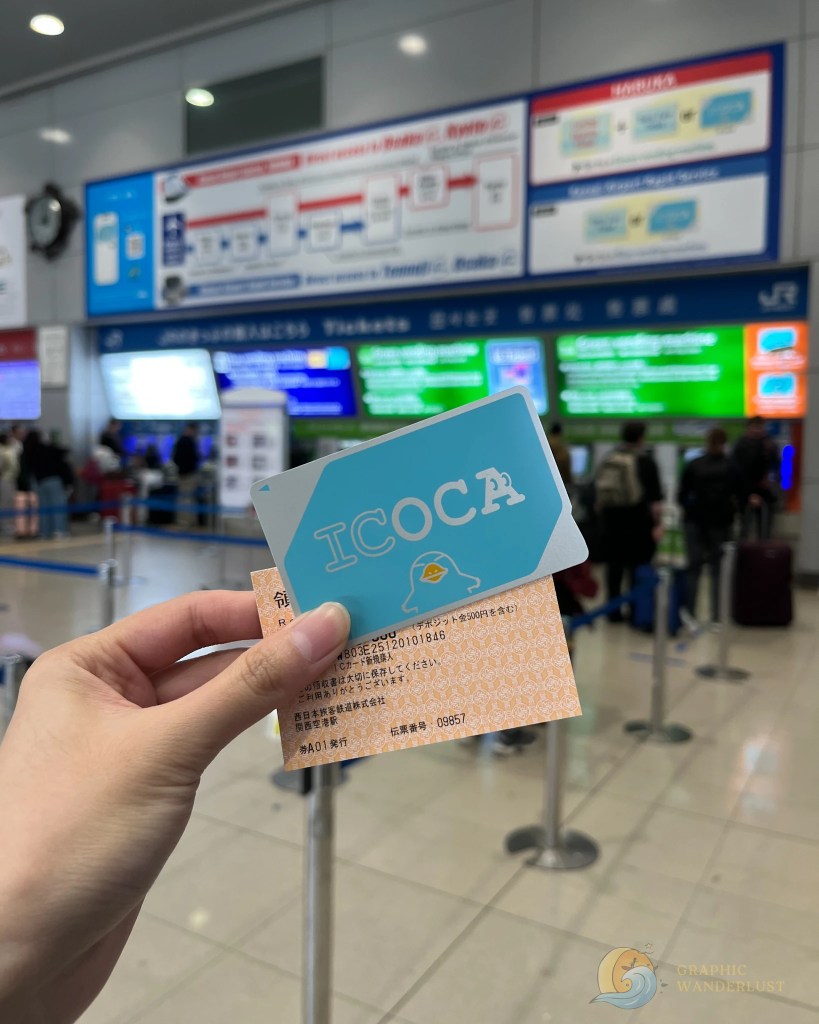 Hand holding a blue ICOCA transit card and an orange ticket in a busy train station