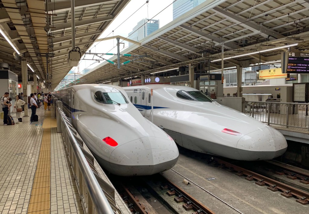 Two white Shinkansen bullet trains at a busy train station platform with passengers waiting