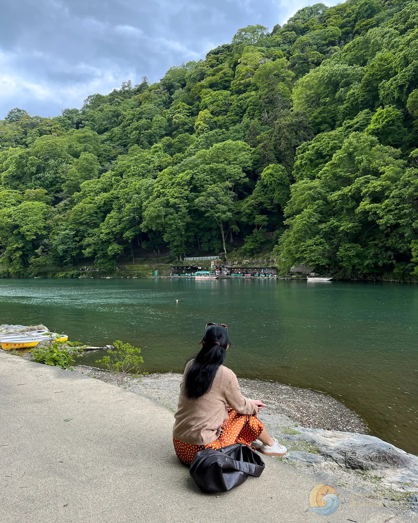 A girl sitting by the river, surrounded by lush greenery and watching the scenery.