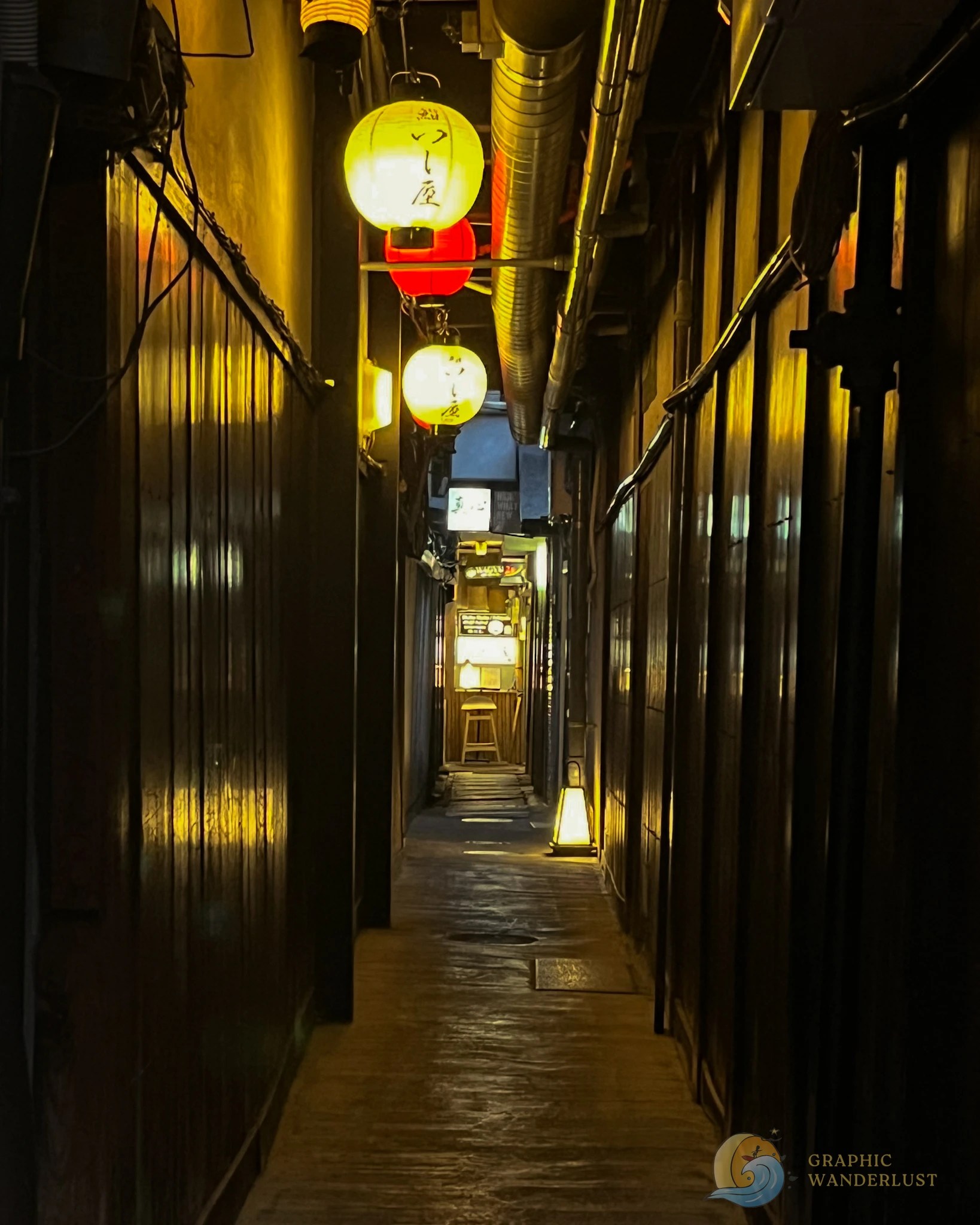 A narrrow alleyway illuminated by lanterns and leading to a small restaurant.