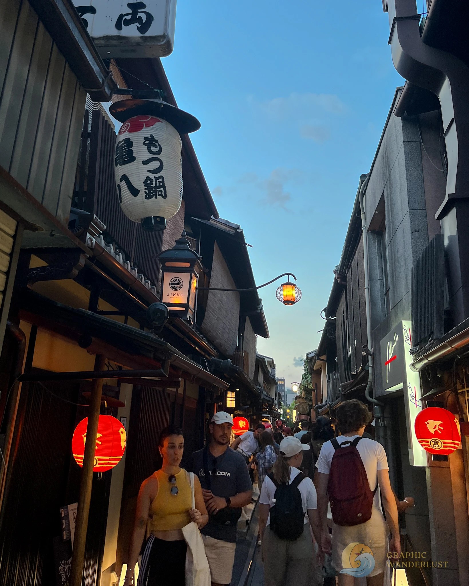 Tourists walking along a narrow alleyway with red lanterns illuminating its street.