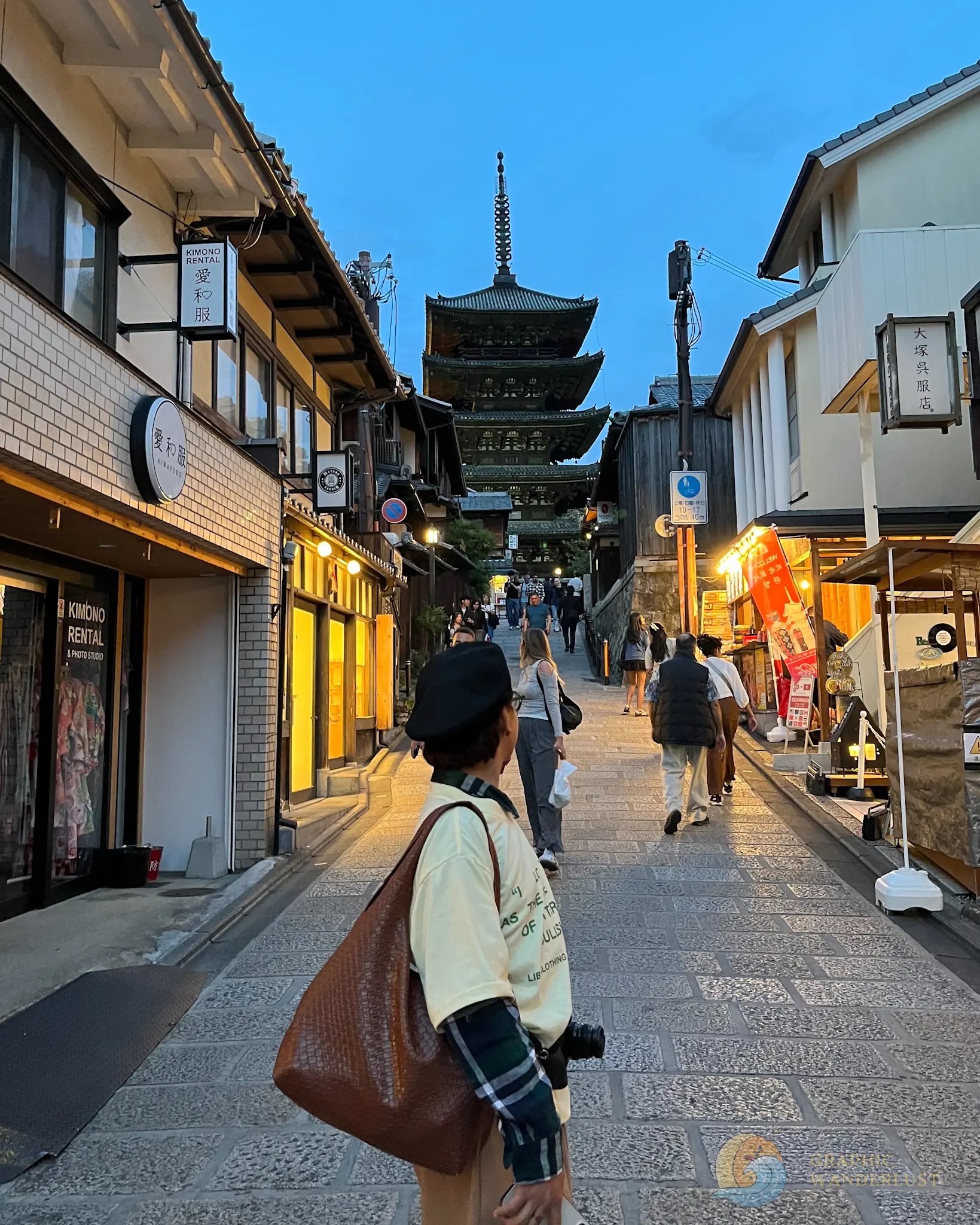 A man looking behind him at a towering old pagoda in a cobblestone street lined with retail establishments.