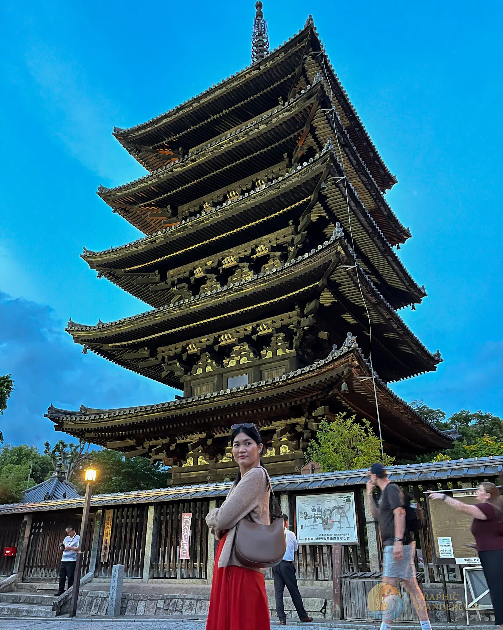 A girl standing infront of a towering old pagoda at night.