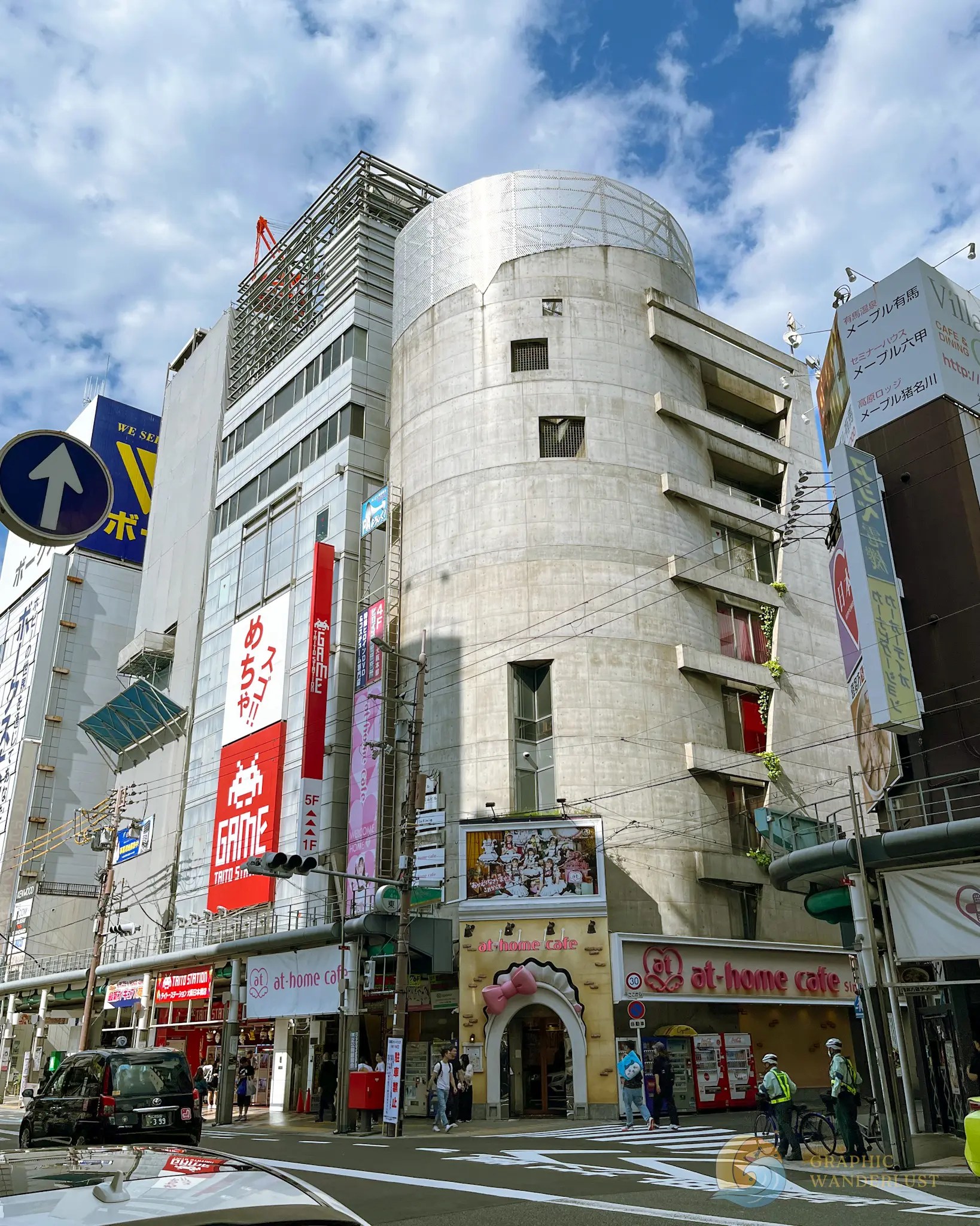 Street view of a busy urban area with tall buildings, advertisements, pedestrians, and vehicles under a partly cloudy sky