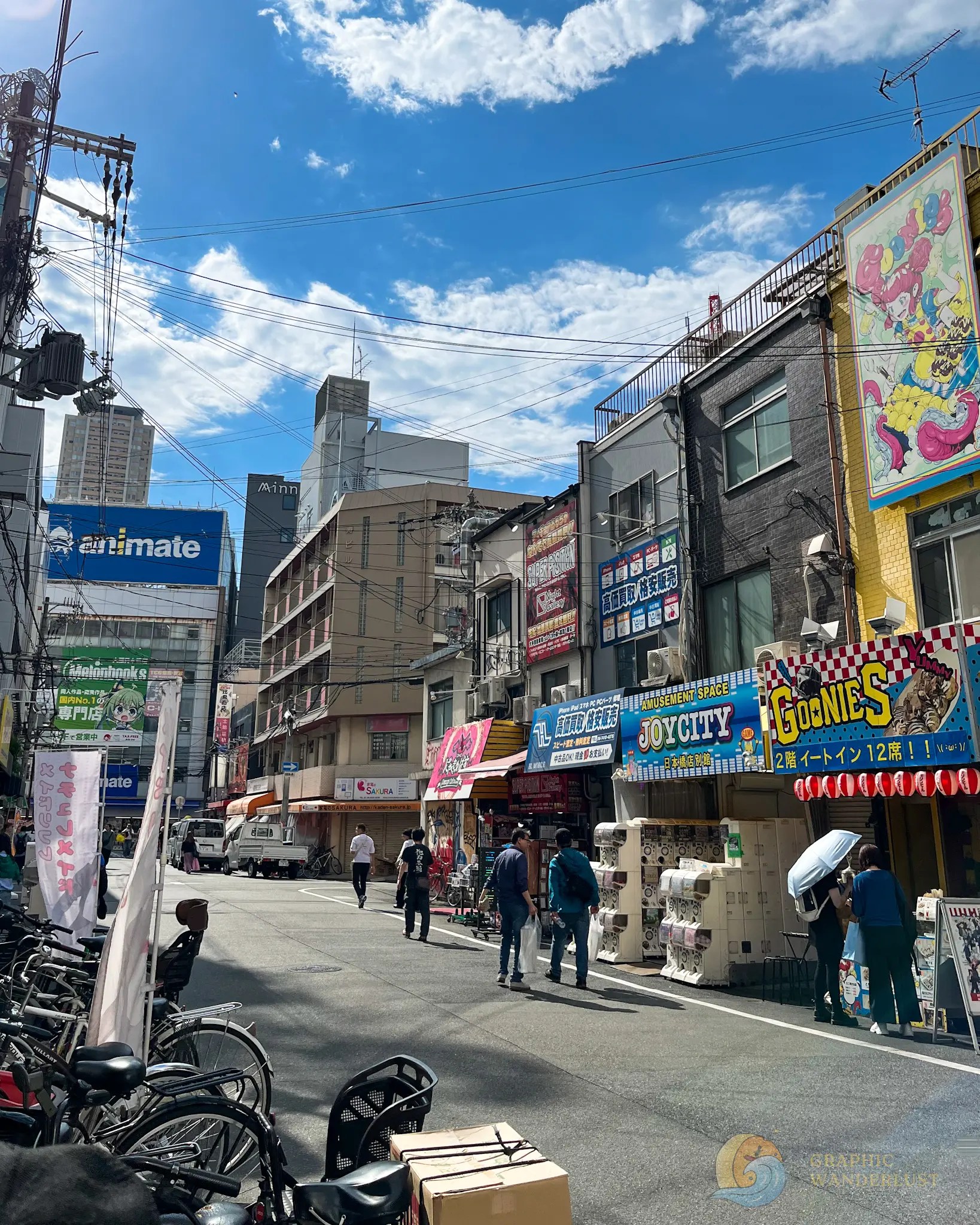 People walking along a busy street lined with colorful signage and bicycles under a blue sky with scattered clouds