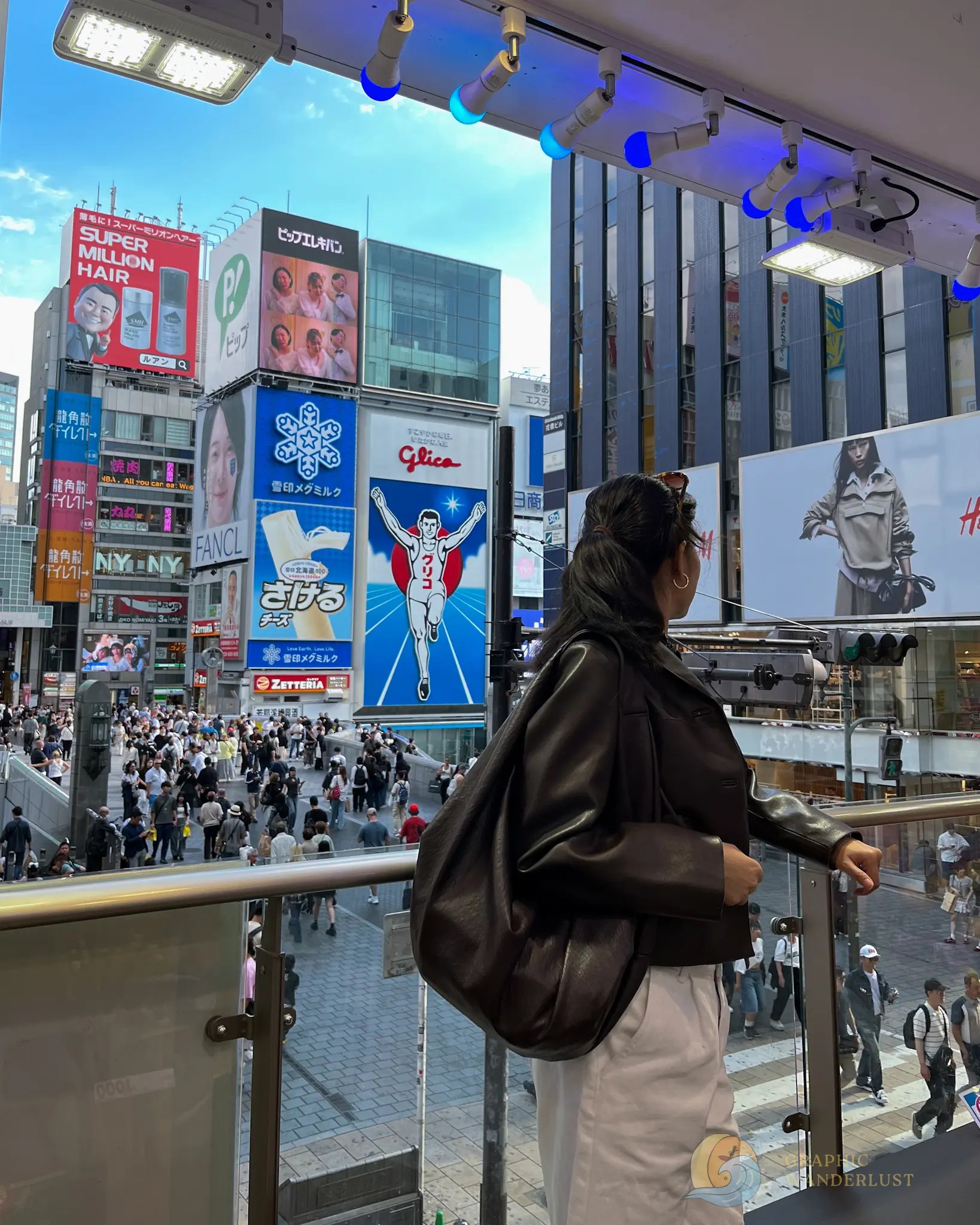 Person wearing a dark jacket and white pants looking out over a busy city street with colorful billboards and crowds