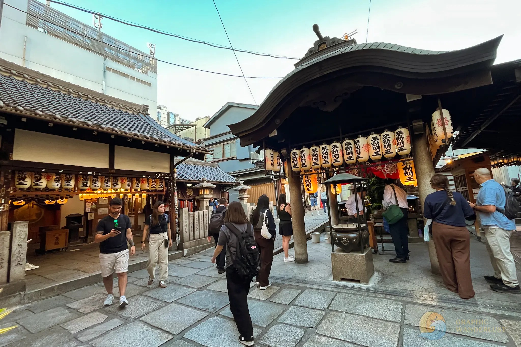 Hozen-ji Temple People walking and standing near a traditional Japanese shrine with hanging lanterns and curved roof structures