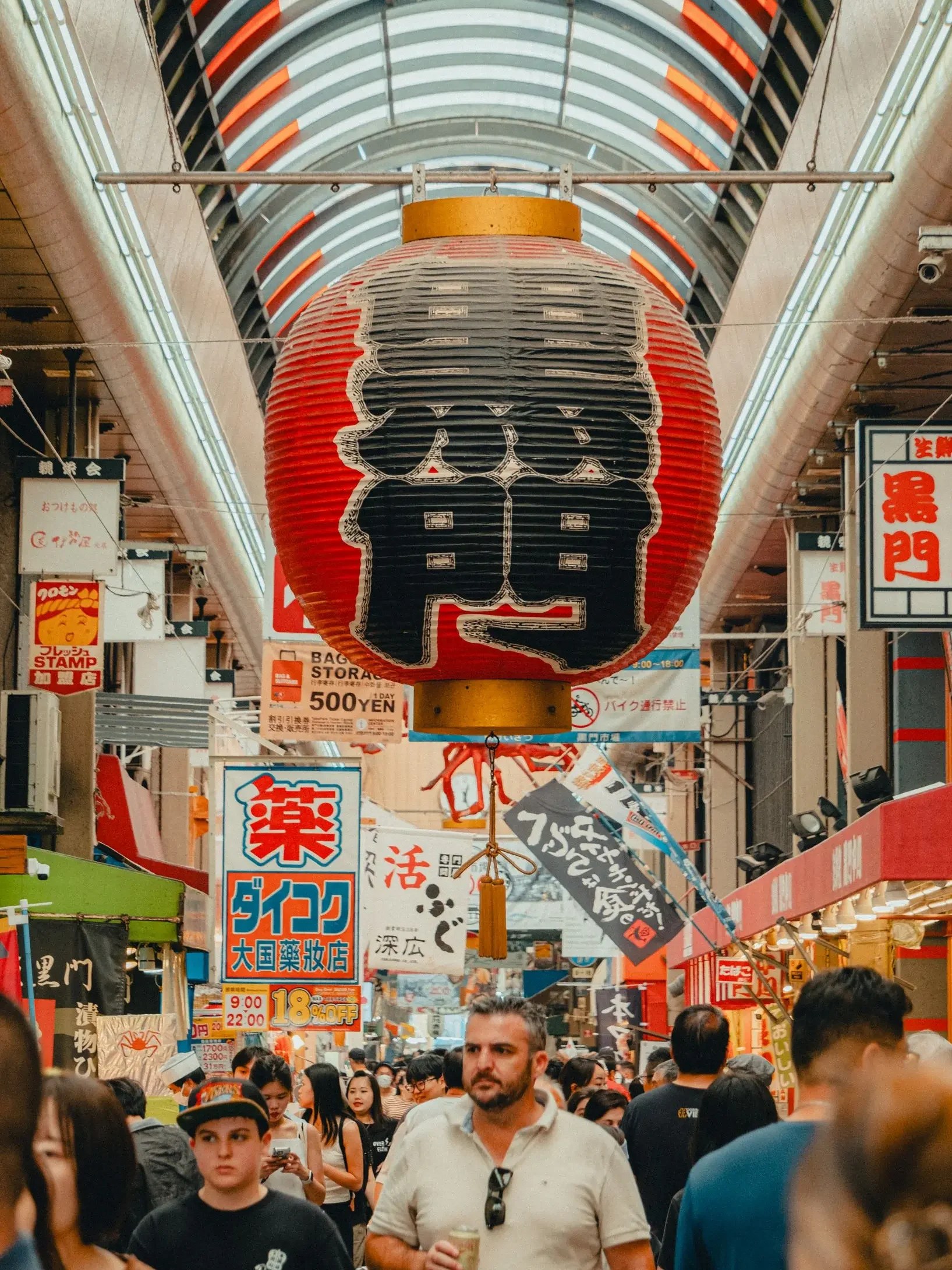 Kuromon Market Large red and black paper lantern hanging in a crowded covered market street with many signs in Japanese and people walking