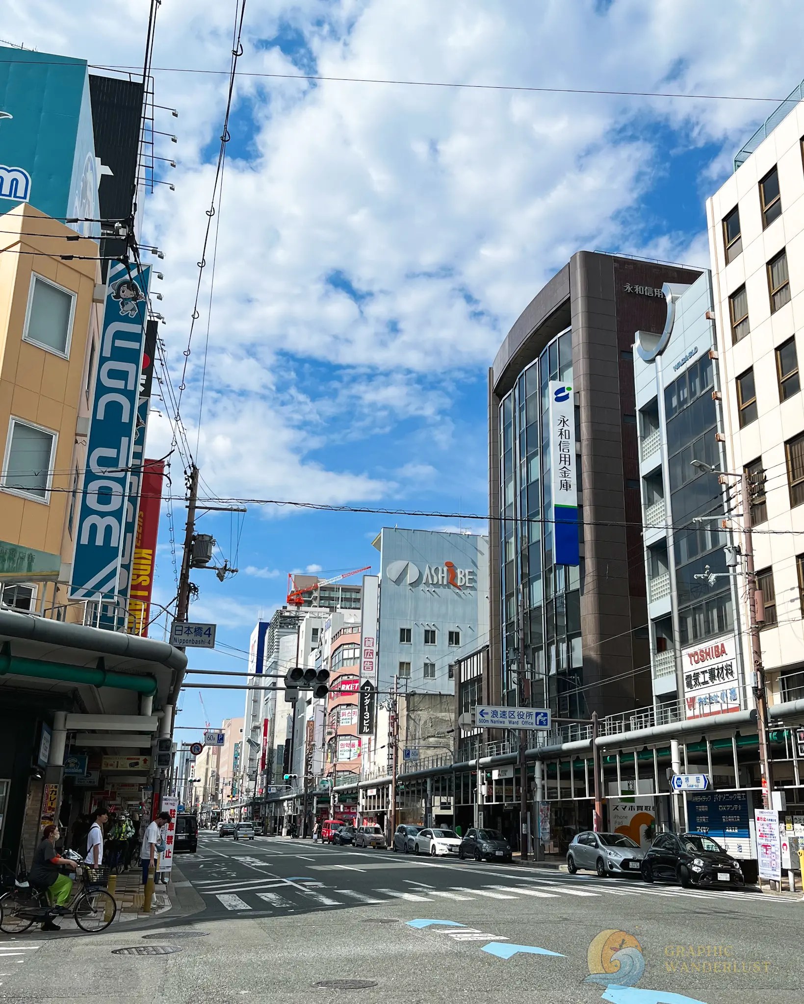 Nipponbashi Denden Town Urban street in Japan with pedestrians, bicycles, cars, and buildings displaying signs in Japanese