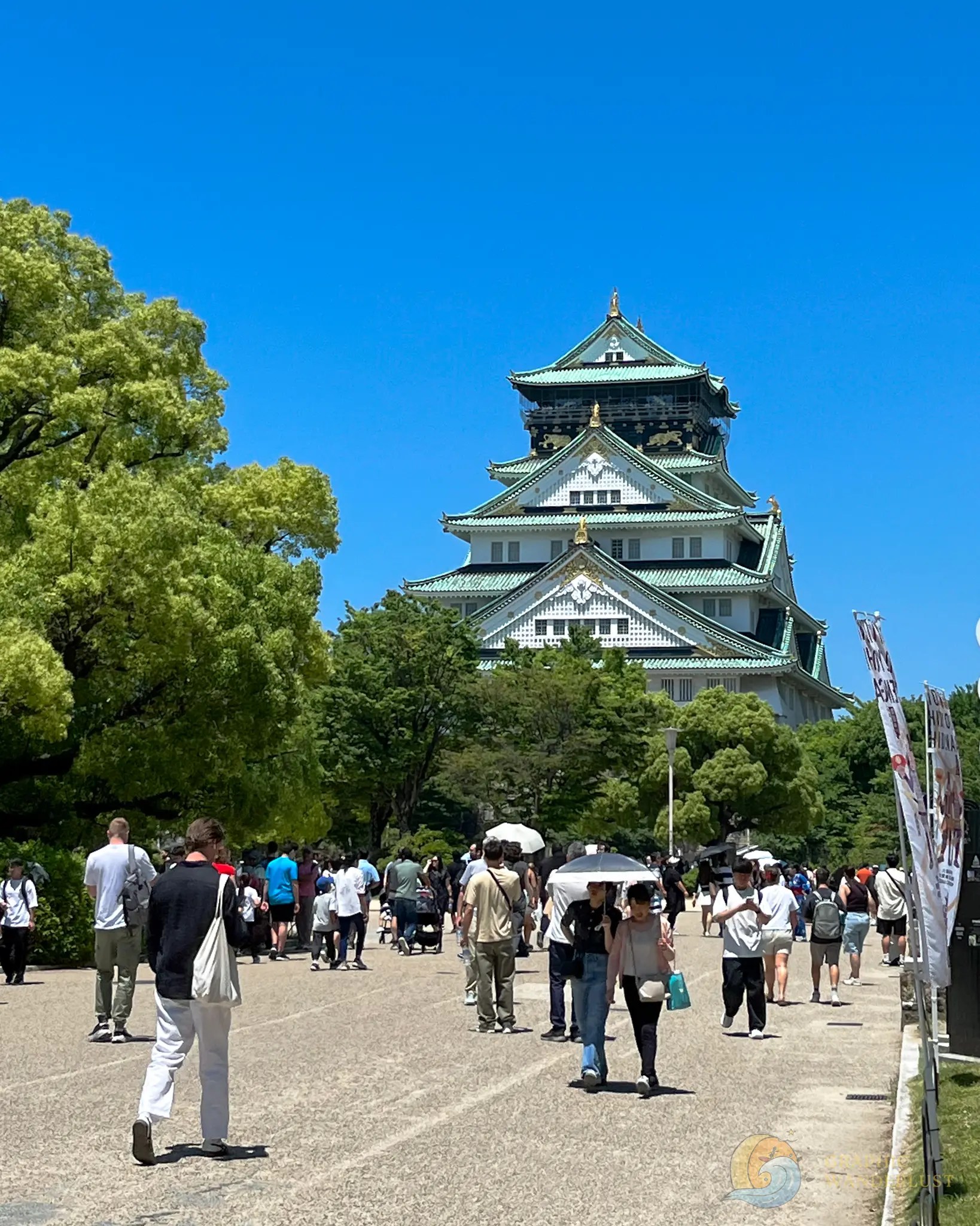 Osaka Castle Park Crowd walking on a path toward a traditional Japanese castle under clear blue sky